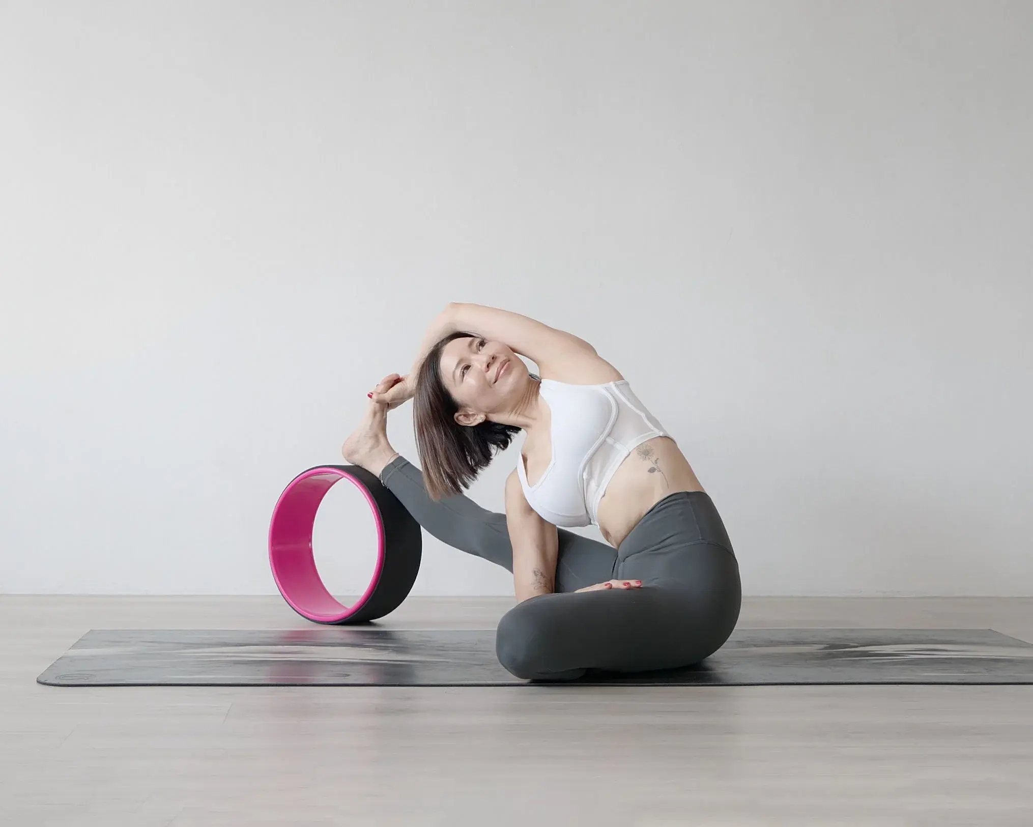 A practitioner in a seated side stretch beside a pink yoga wheel